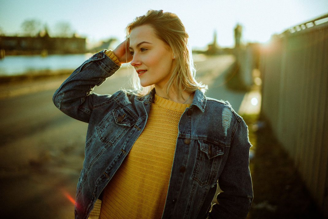 Gegenlichtaufnahme einer jungen Frau mit Jeansjacke und gelben Pullover