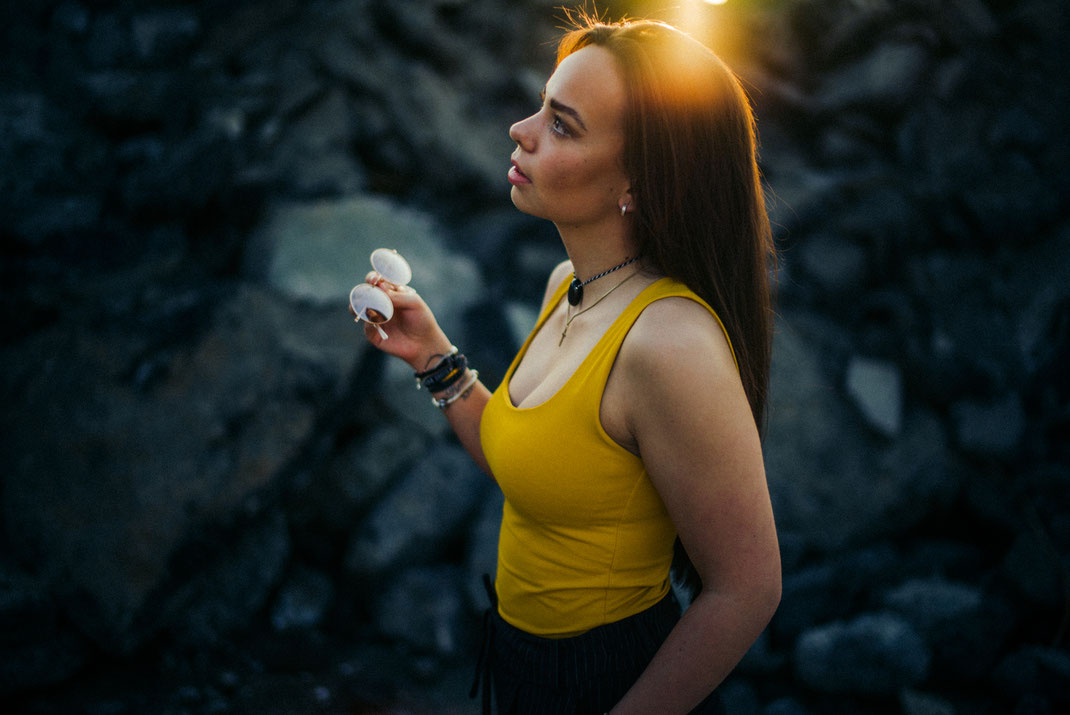 Junge Frau im Gegenlicht hält ihre Sonnenbrille fest