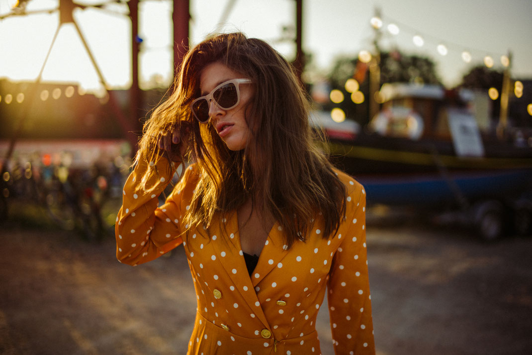 Frau mit Sonnenbrille schaut zur Seite im Hintergrund Lichterketten und die Sonne