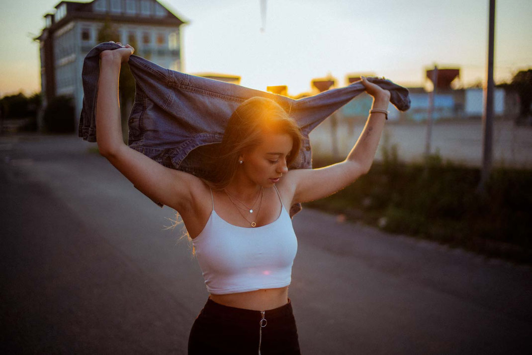 Junge Frau hält ihre Jeansjacke mit beiden Händen fest und streckt dieses in die Höhe
