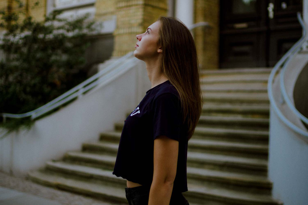 Frau mit bauchfreiem Outfit schaut in die Himmel im Hintergrund eine Treppe