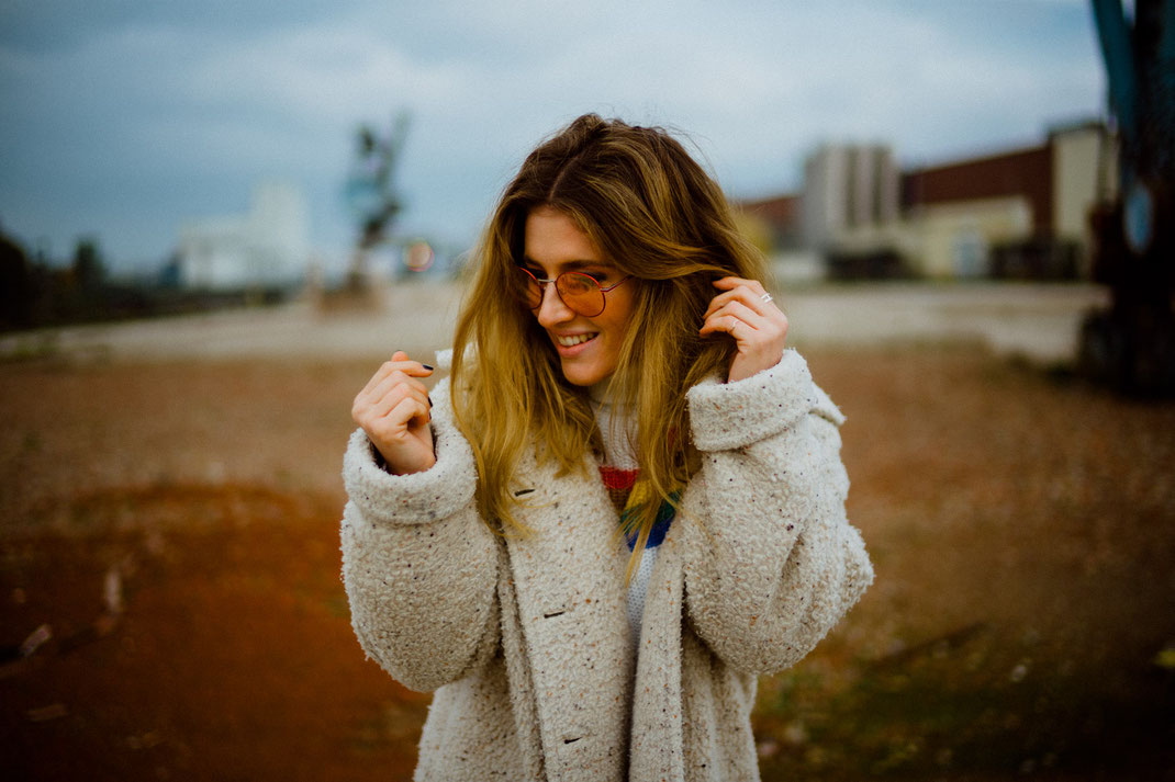 Lächelnde junge Frau mit Mantel und stylischer Sonnenbrille beim Fotoshooting