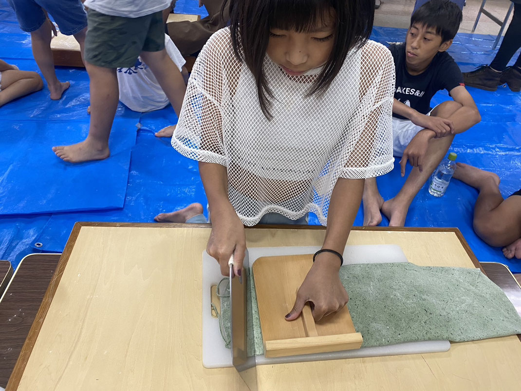 飛騨朝日のよもぎうどん手づくり体験で女の子が専用包丁を使い丁寧に手打ちうどんを切っている様子