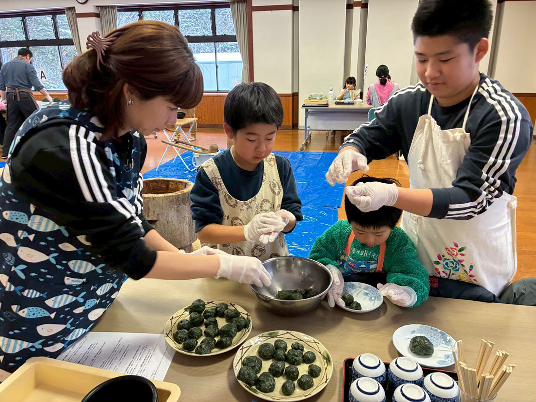飛騨あさひのよもぎ餅つき体験で、笑顔の父親と子供が一緒につきたての緑鮮やかなよもぎ餅を丸めて成形している様子。道の駅ひだ朝日村の明るい研修室での体験風景。