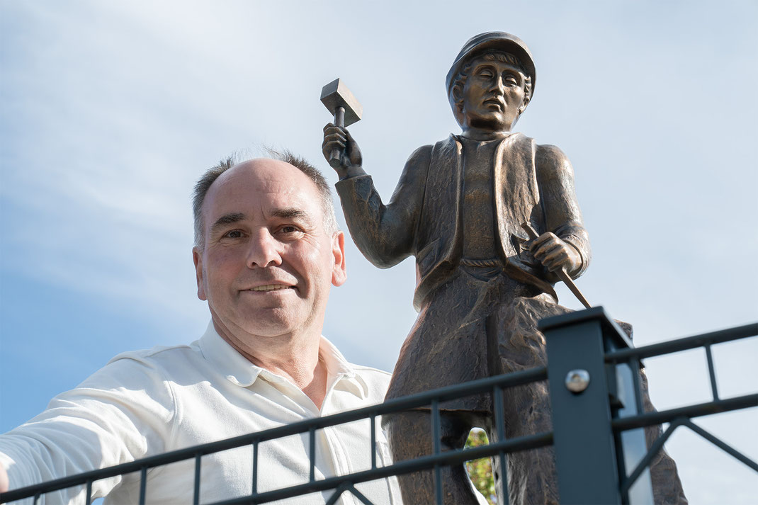 Foto des Firmeninhabers Rolf Bell vor der Bronzestatue eines Steinmetzes