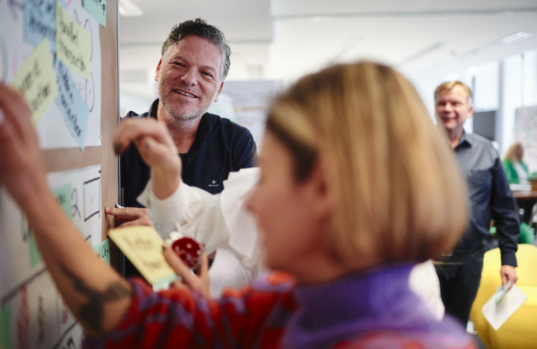 Event-Foto vom Mercedes-Benz Global Training: Teilnehmende kleben Notizzettel an ein Poster – eine interaktive Übung im Workshop. Der Austausch ist lebendig, die Stimmung fokussiert und freundlich.