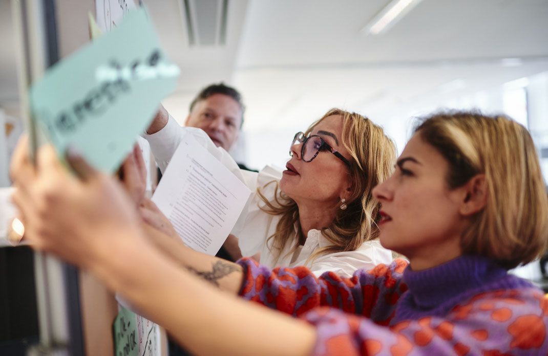 Event-Foto vom Mercedes-Benz Global Training: Drei Teilnehmende arbeiten konzentriert an einer Pinnwand und heften Kärtchen mit Begriffen an – eine dynamische Übung zum Thema Werte und Kommunikation.