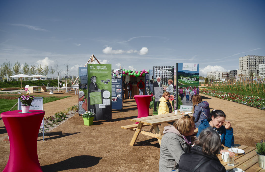 Eventfoto von Christoph Bastert: Ausstellung der LandFrauen Württemberg-Baden auf der BUGA Mannheim 2023 mit Infotafeln, Blumen, Sitzgruppen und Besucherinnen bei sonnigem Wetter.