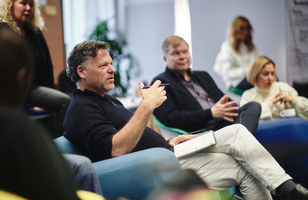 Ein Mann spricht während eines Trainings von Mercedes-Benz Global Training in Stuttgart, umgeben von Kolleginnen und Kollegen in entspannter Workshop-Atmosphäre. Foto: Christoph Bastert.