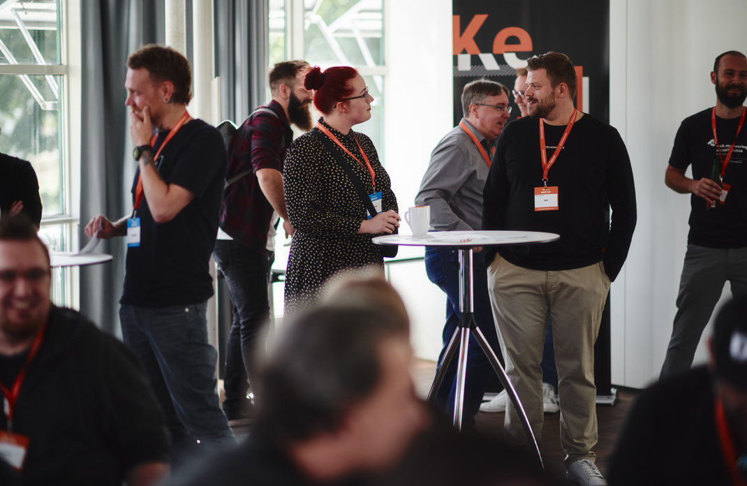 Event Foto vom BAR-CAMP 2022 der KELLERKINDER: Teilnehmende stehen und unterhalten sich an Stehtischen im offenen Workshopbereich.