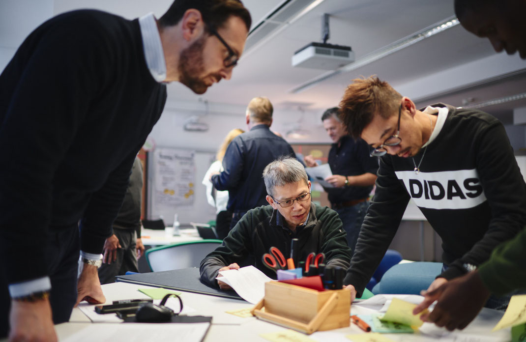 Event-Foto vom Mercedes-Benz Global Training: In intensiver Gruppenarbeit beugen sich mehrere Teilnehmende über den Tisch, tauschen sich aus und sortieren gemeinsam Materialien – konzentrierte Teamarbeit in Aktion.