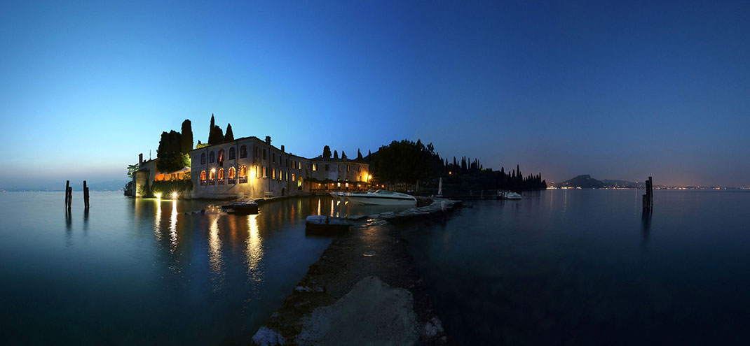 Illuminated classical building with pier and boats at Lago di Garda, lake in Italy at night, 1280x750px