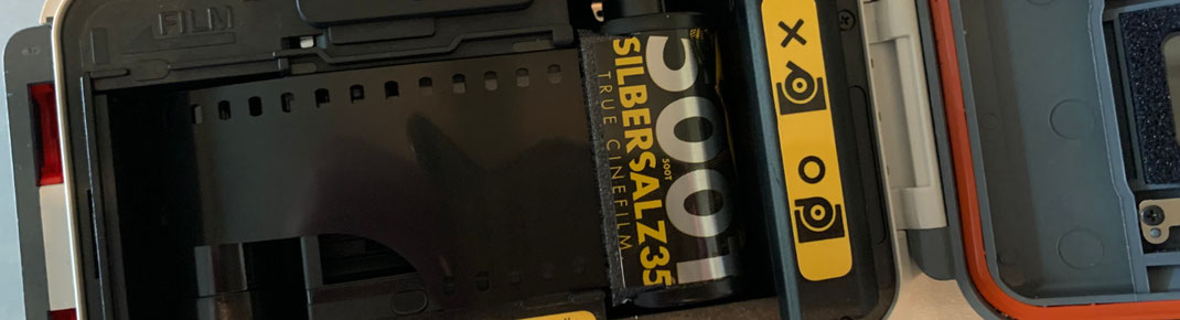 Eine Nahaufnahme der geöffneten Rückseite einer analogen Unterwasserkamera. Im Inneren ist eine Filmrolle der Marke „Silbersalz35 500T“ eingelegt, deren Filmstreifen über das Bildfenster gespannt ist.