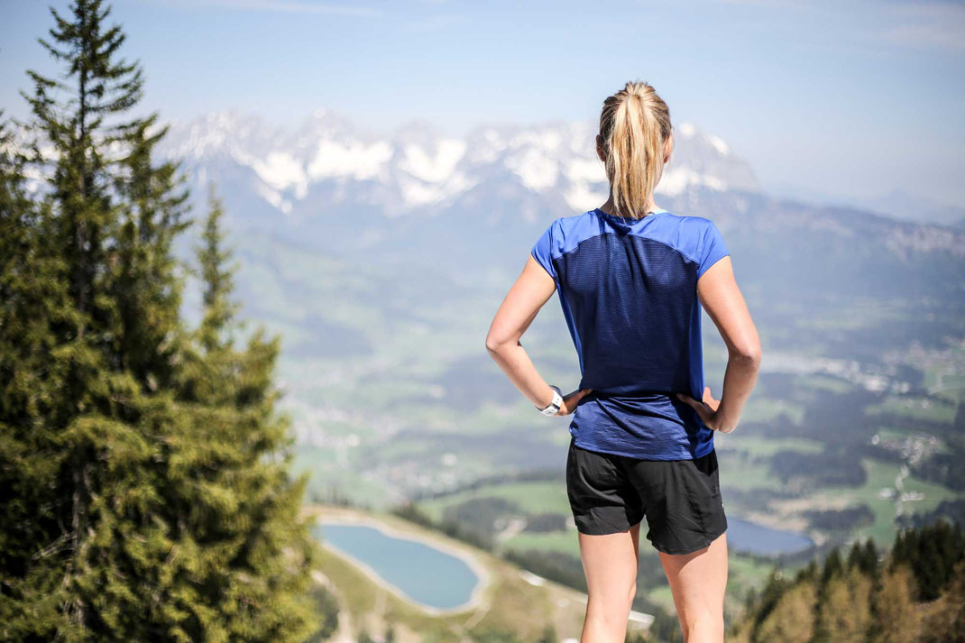 Trailrun am Berg mit Blick hinab ins Tal und zu einem Bergsee in der grünen Natur