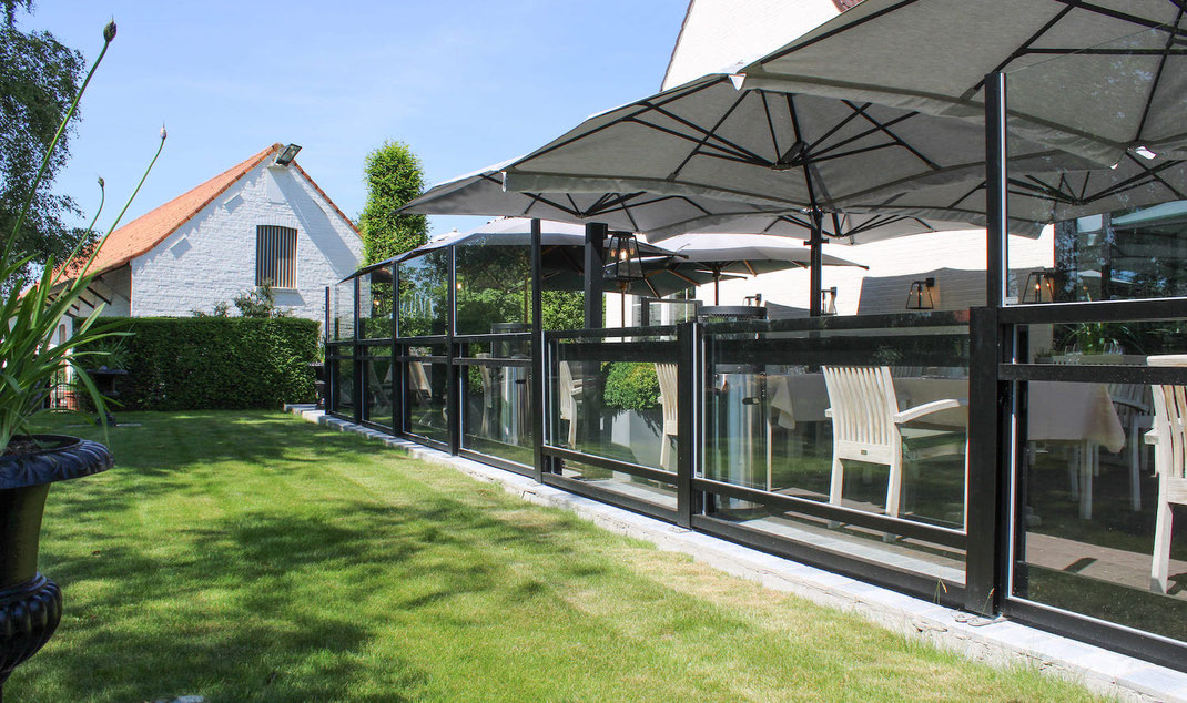 harmonische Abgrenzung einer Restaurant-Terrasse zum Gartenbereich durch ein lückenloses in der Höhe verstellbares Windschutz-System-Sytem