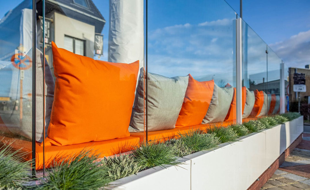 Komfortable Terrasse: Casablanca Windschutz-Sitzbank mit leuchtenden bequemen orangen Kissen und integrierter Gräser-Bepflanzung