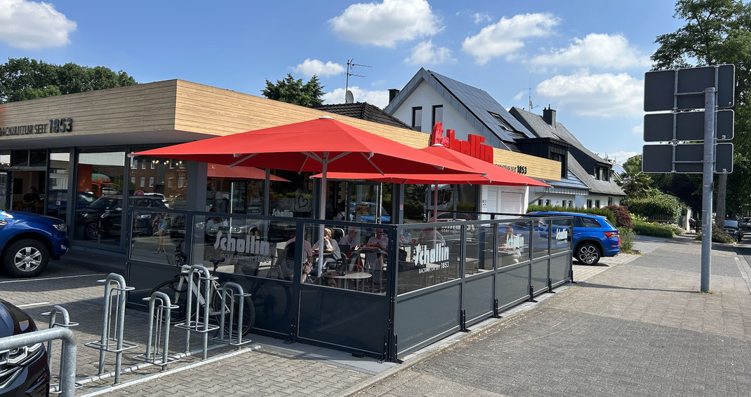Große Bäckerei-Filiale mit geschütztem Außenbereich, rotem Sonnenschirm und festen Windschutz-Glaswänden