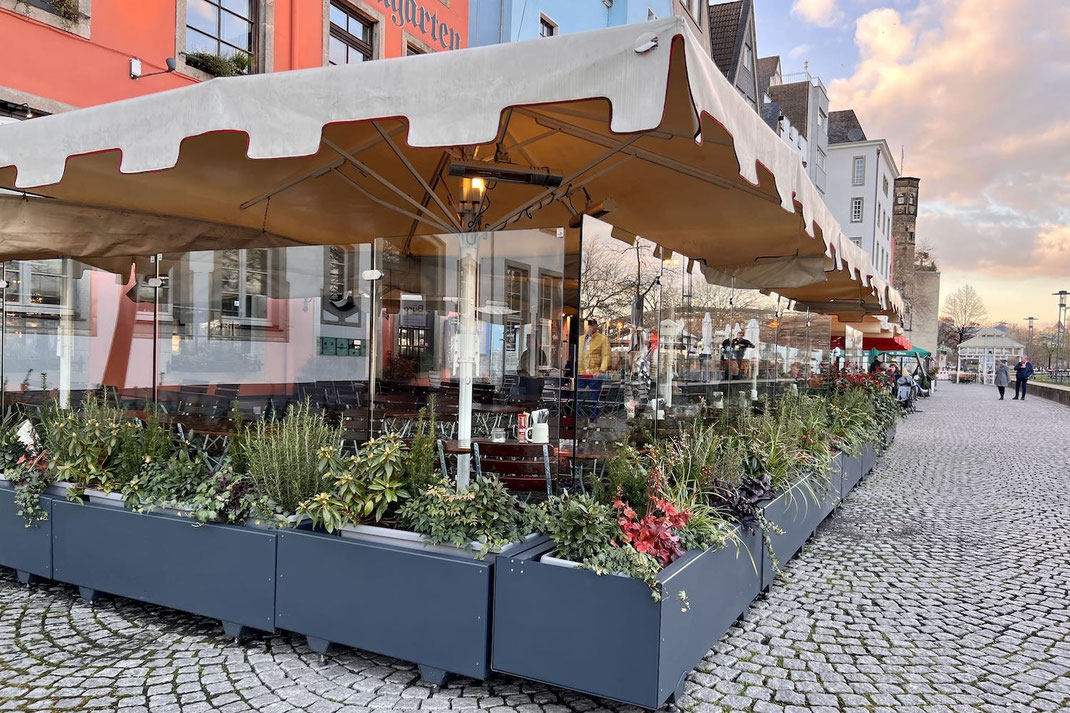 Terrassenabgrenzung mit Glas-Windschutz und bepflanzten anthrazitfarbenen Sockelmodulenüberdacht durch eine große Markise