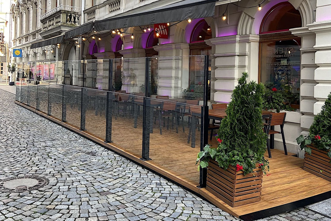 Glas-Balustrade als Absturzsicherung auf einem Gastro-Podest – transparenter Windschutz kombiniert mit einem Holzpodest