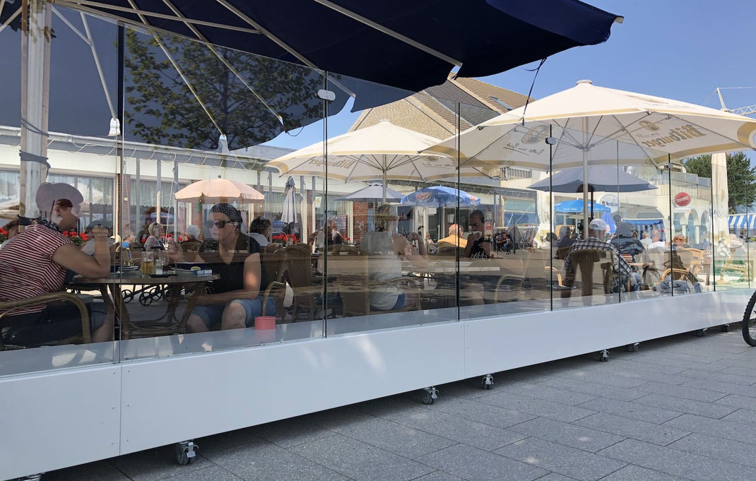 Gläserne Terrassenabtrennung mit integrierter Sitzbank auf feststellbaren Rollen für die Außengastronomie