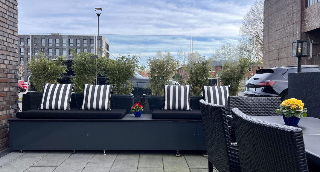 Casablanca Windschutz-Modul mit integrierter Sitzbank, dunklen Polstern und Gräser-Bepflanzung auf exklusiver Terrasse an einem Hotel