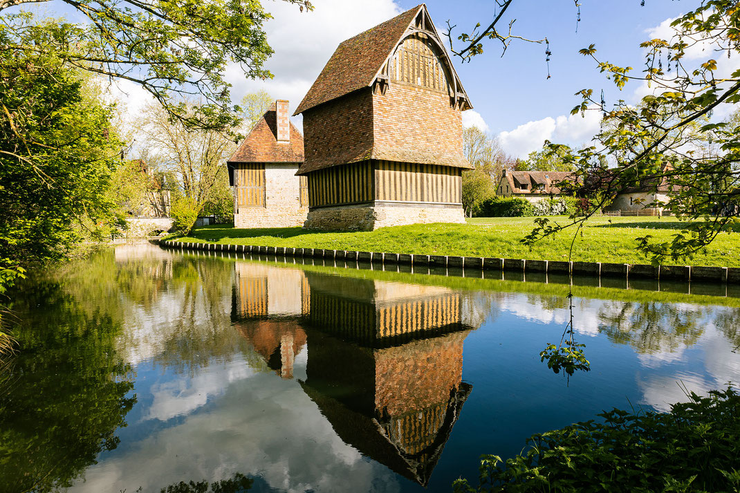 Die Wirtschaftsgebäude des Château Crèvecœur in der Normandie spiegeln sich im Burggraben