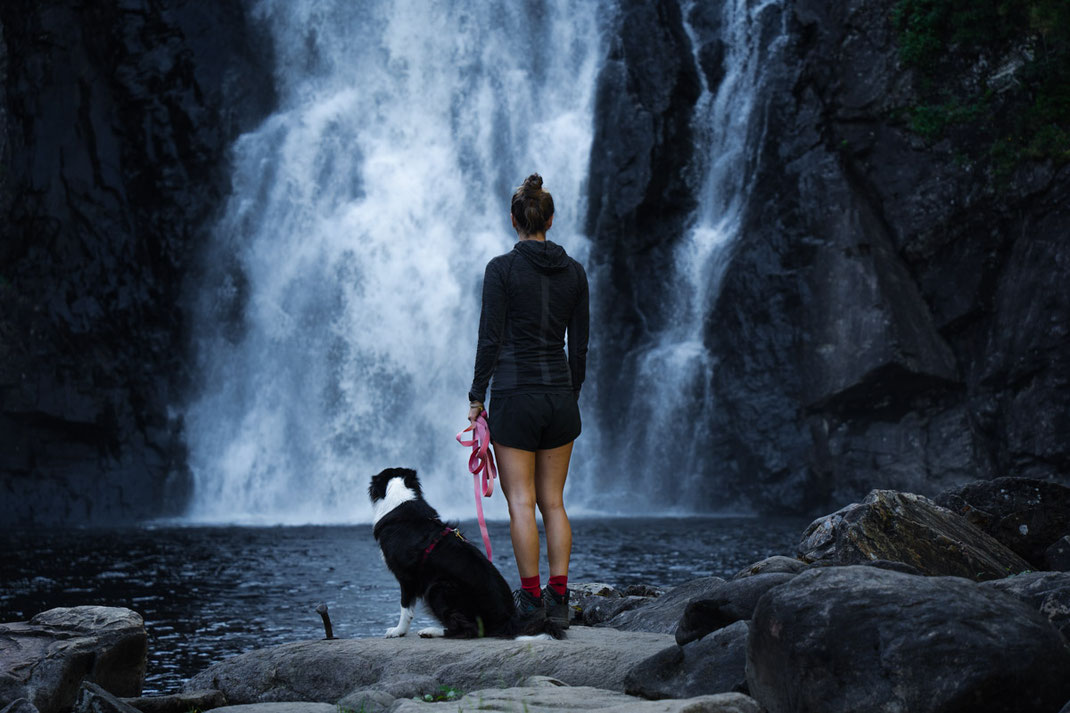 Eine Frau bestaunt mit ihrem Hund den Storfossen Wasserfall.