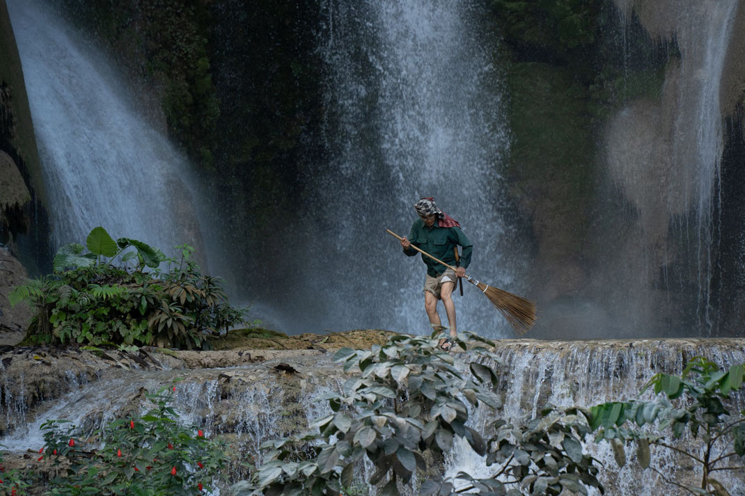 Un hombre al pie de la cascada de Tat Kuang Si con una escoba.