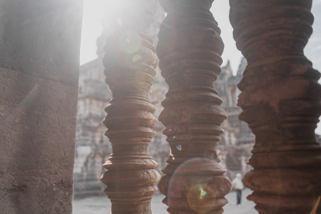 The sun shines through stone pillars at Angkor Wat.