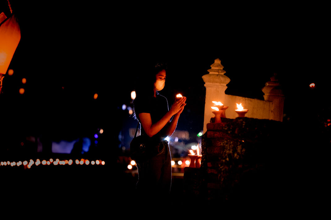 Une femme allume une bougie et prie dans les ruines de Sukhothai.