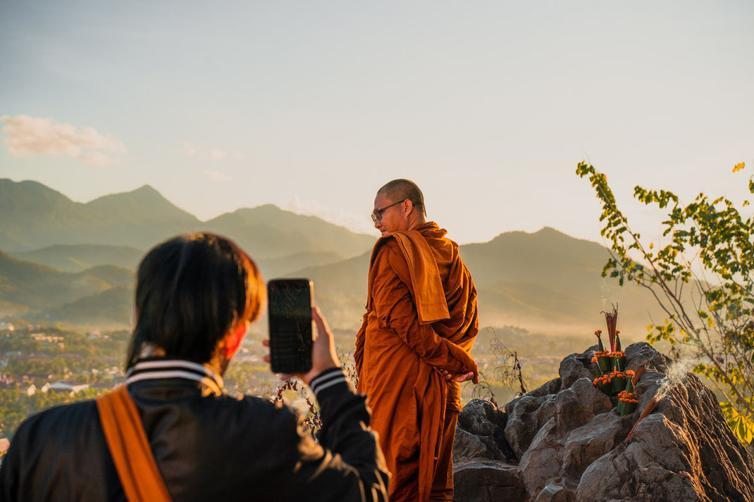 夕暮れの岩の上に立ち、写真を撮られる僧侶。