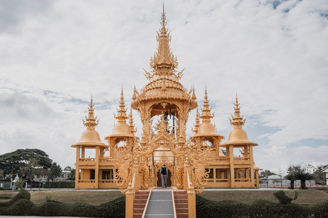 Ein goldener Tempel mit einen Mann in der Nähe des Weißen Tempels in Chiang Rai.