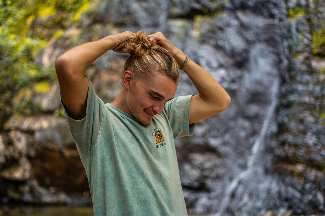 A man in a green T-shirt ties his hair into a ponytail.