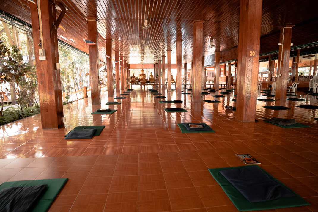 Eine große Halle mit verteilten Kissen und Büchern in Wat Pa Tam Wua Kloster.