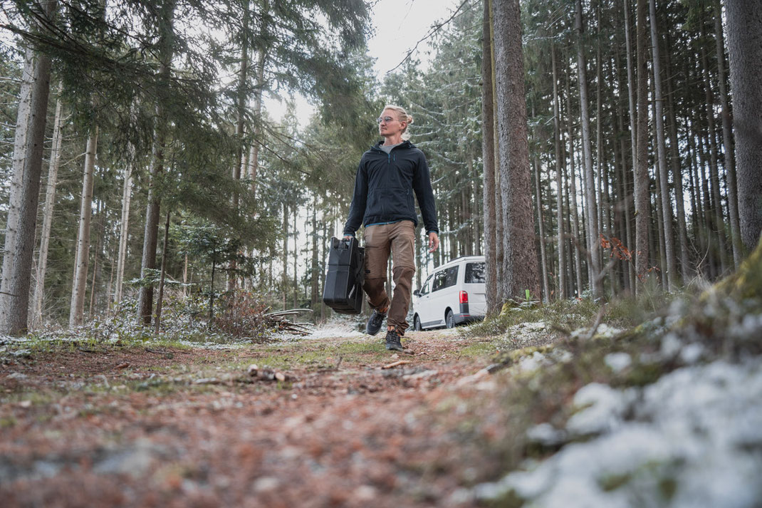 Ein Mann mit einem schwarzen Kanister geht durch den Wald.