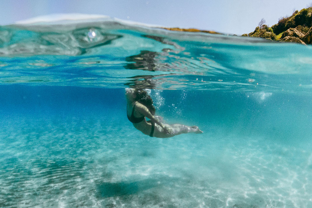 Unterwasseraufnahme einer tauchenden Frau im türkisen Wasser.