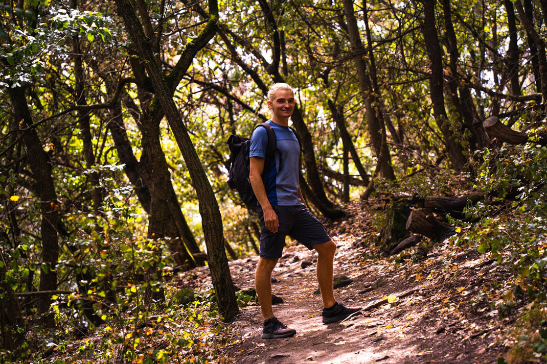 Ein Mann steht auf einem Wanderweg im grünen Wald und blickt in die Kamera.