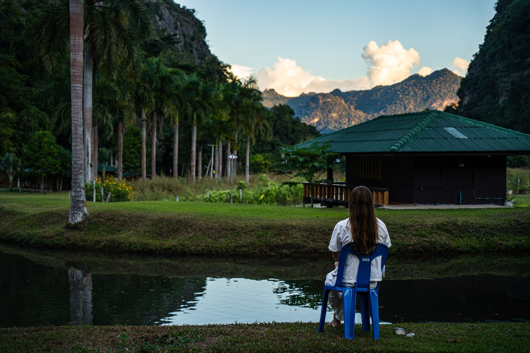 Eine Frau mit langen braunen Haaren sitzt auf einen blauen Stuhl und beobachtet den Sonnenaufgang.