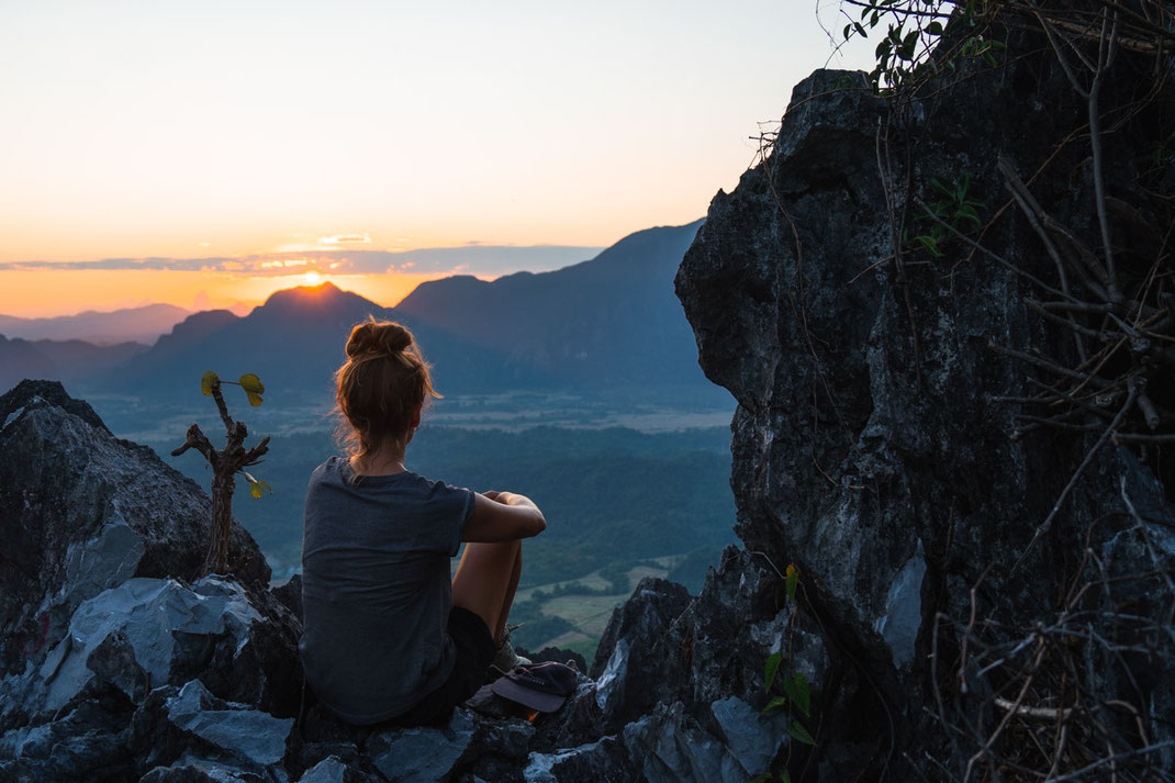 Une femme est assise à un point de vue et regarde la ville de Vang Vieng au coucher du soleil.