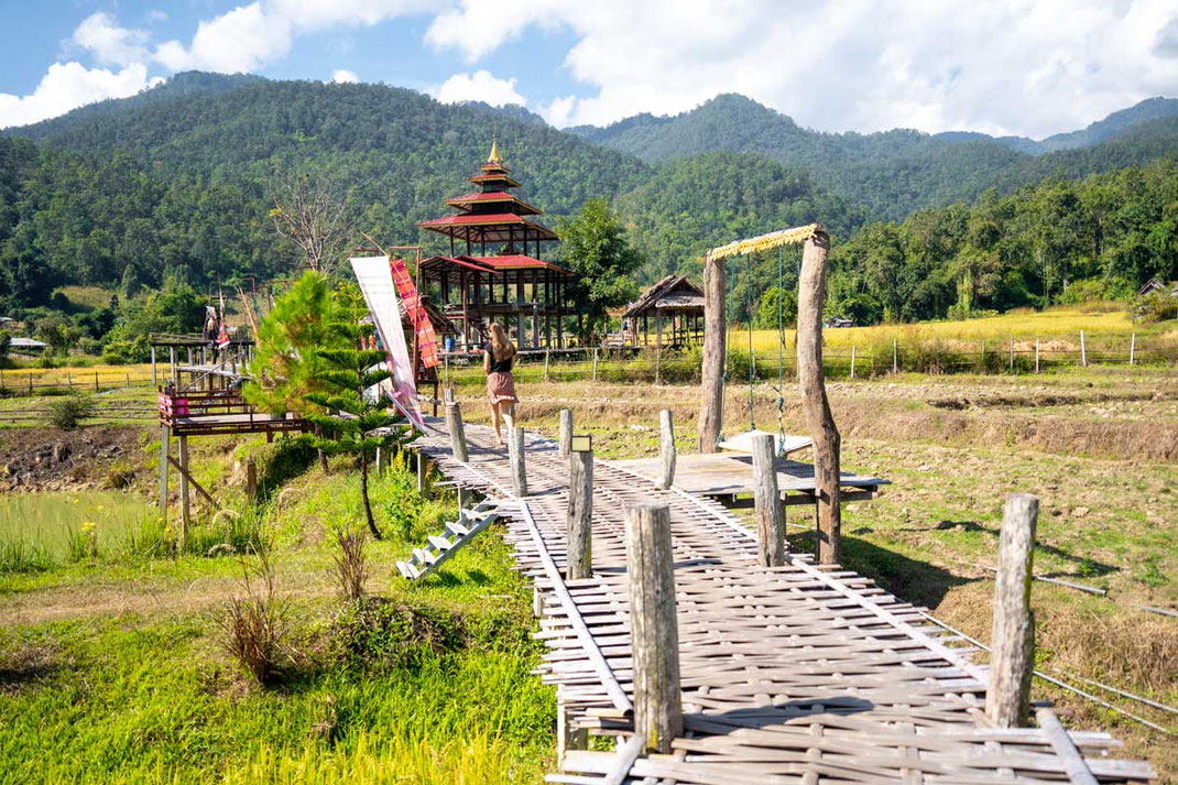 A woman walks on a wooden bridge through the rice fields in Pai.