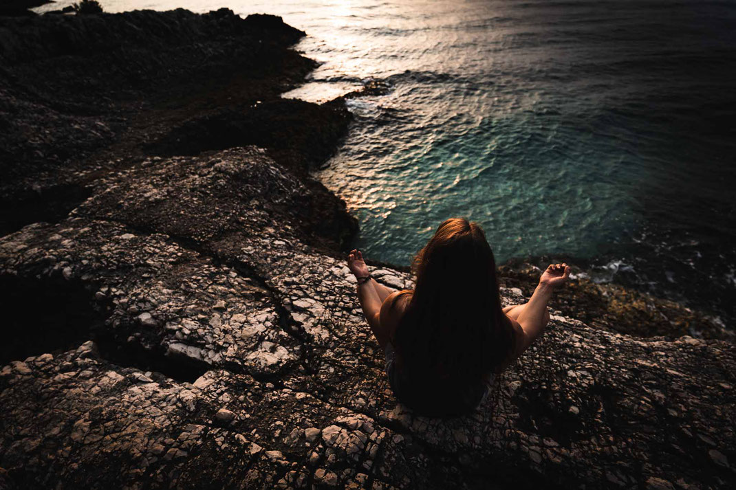 Meditierende Frau an der felsigen Küste der Blauen Lagune während des Sonnenuntergangs.