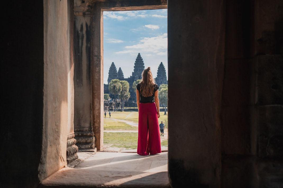 A woman in red pants stands in front of the landmark of Cambodia.