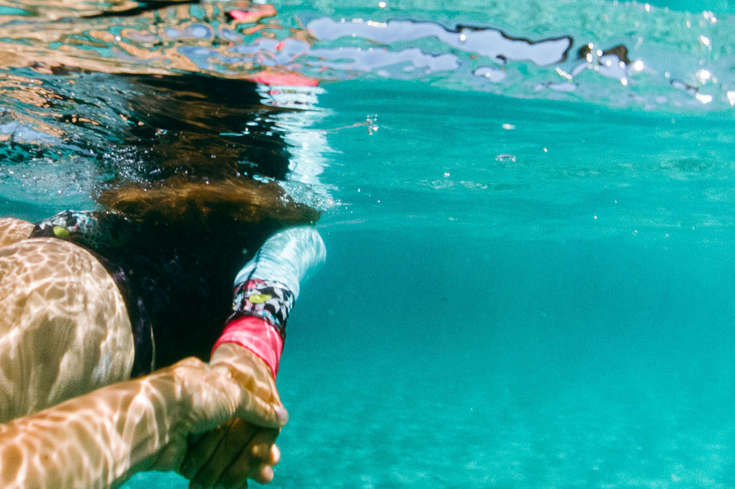 Unterwasseraufnahme einer tauchenden Frau, die im türkisen Wasser dem Fotografen die Hand gibt..