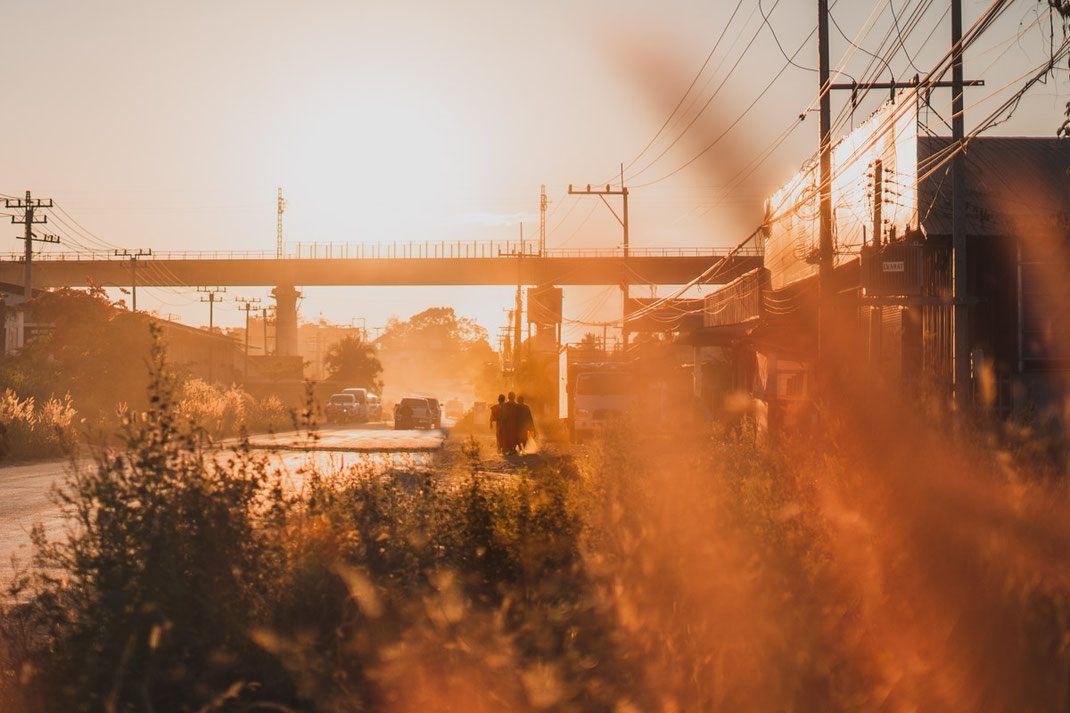 Three monks walk towards the sunset on a dusty street in Luang Prabang.