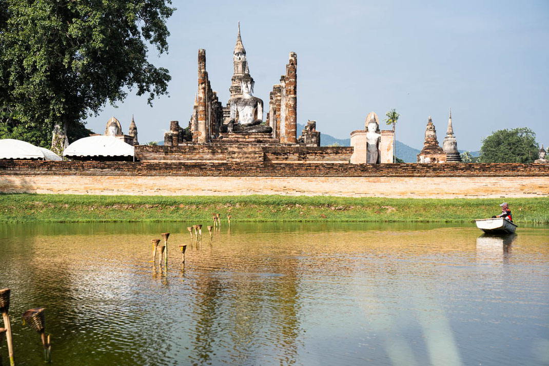 Un ancien temple avec un bouddha assis se trouve juste à côté d'un lac à Sukhothai.