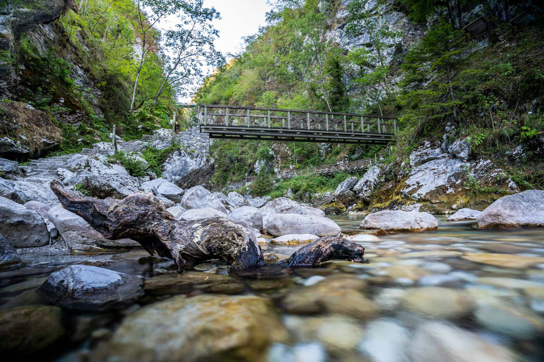 Langzeitbelichtung der malerischen Tolmin Klamm mit Felsen, Fluss, Bäumen und einer Holzbrücke.