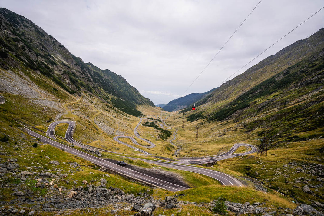 Die kurvige Transfogarascher Hochstraße mit einer roten Gondel im Hintergrund.