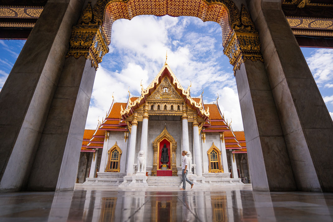 L'homme traverse le temple de Wat Ben, passe devant les colonnes de marbre et les statues de Bouddha.