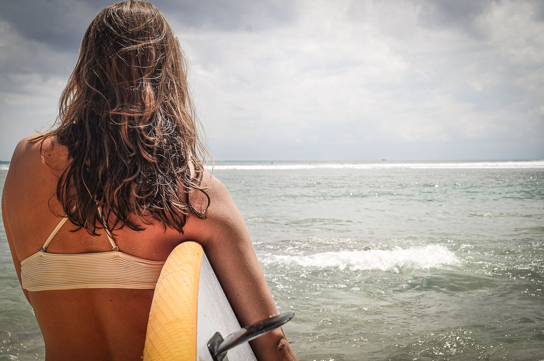 サーフボードを小脇に抱えて海を眺める女性。