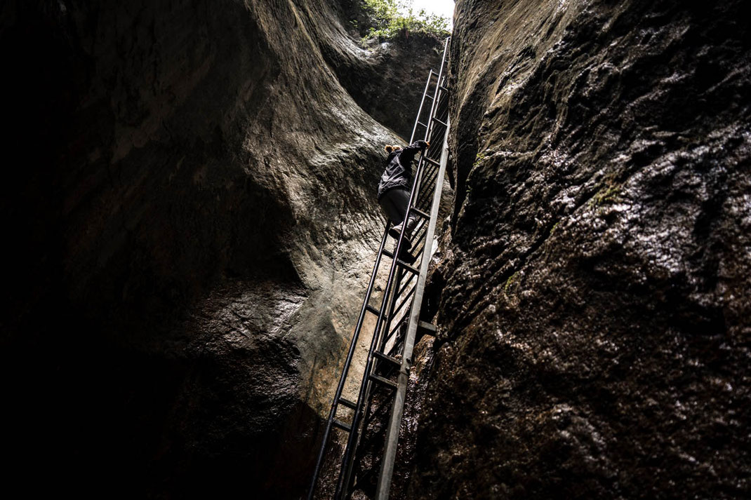 Eine Person klettern an einer Leiter aus dem dunklen Canyon nach oben.